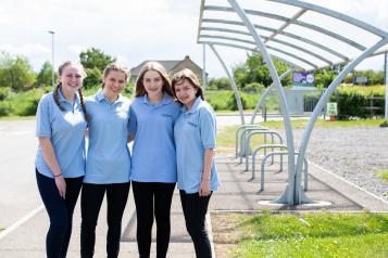 Four girls stood outside a bike shed in a line with their arms round each other