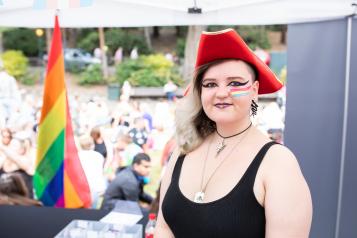 Woman in a red hat stood in front of a multicoloured flag