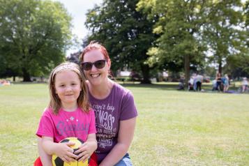 Mum kneeling on the grass with her arms round a young girl