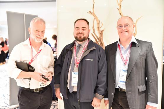 Three men stood discussing something at a conference